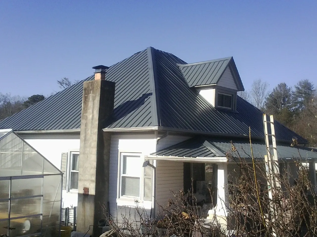 Dark blue standing seam metal roof on a white farmhouse with dormer — Slate & Tile Roof Repair by Roofing Brothers in Katy