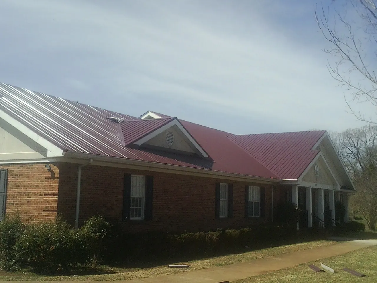 Red metal roof with gabled entries on a long brick building, from a Hail Damage Roof Repair job in Katy