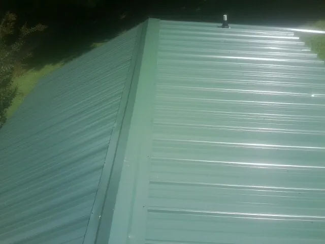 New green metal panels meeting at the ridge of a roof — Flat Roof Repair work by our crew in Katy