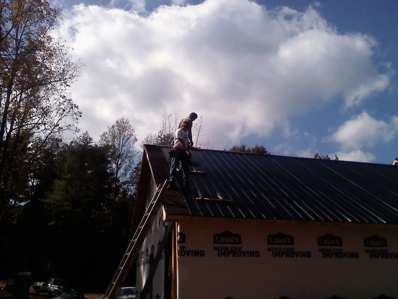 Roofer fastening dark metal panels high against a cloudy sky, from a Roof Inspection job in Katy