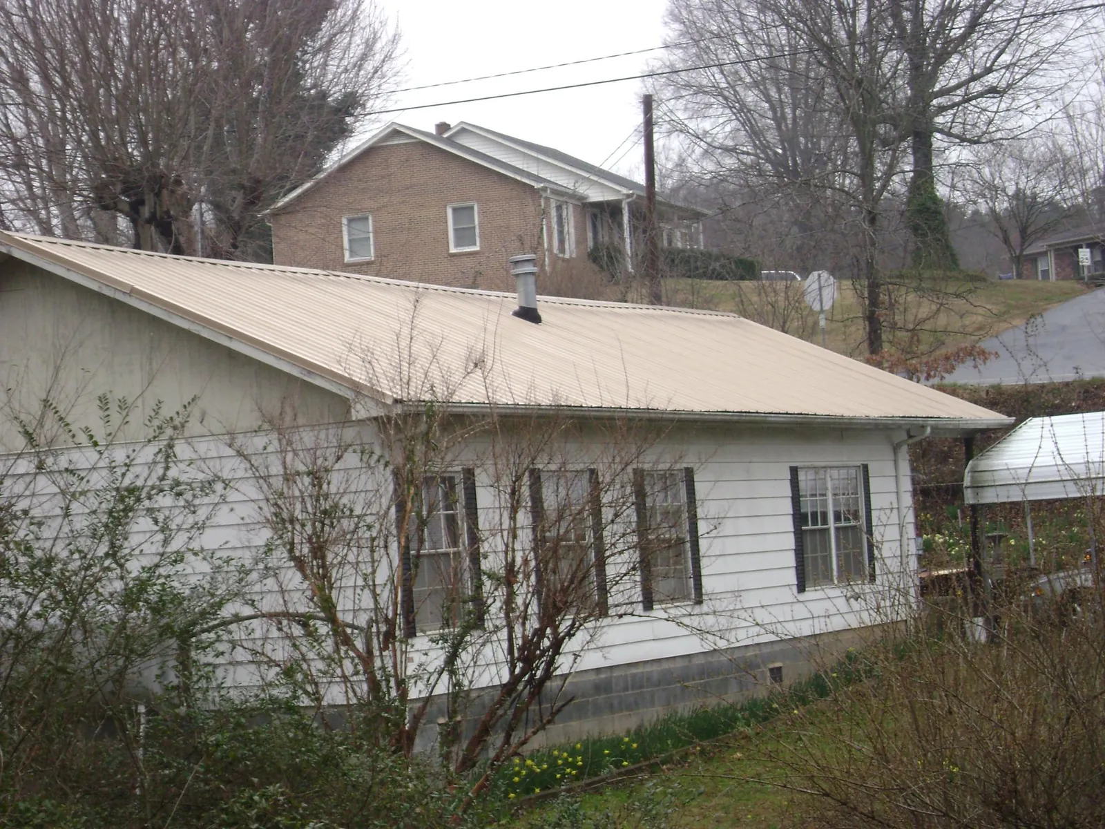 Tan metal roof on a white sided house set into a hillside — Commercial Roofing by Roofing Brothers in Katy